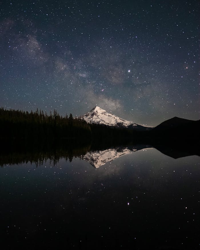 Snow-capped Mount Hood reflected in a serene lake under a starry sky, Oregon.